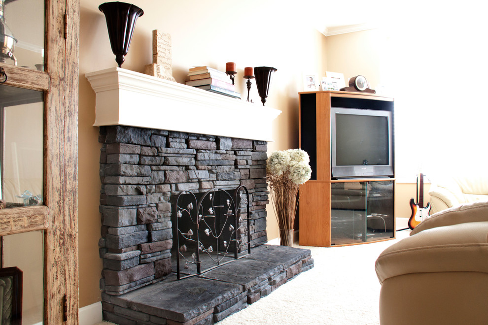 バンクーバーにある中くらいなトラディショナルスタイルのおしゃれなリビング (ベージュの壁、カーペット敷き、標準型暖炉、石材の暖炉まわり、据え置き型テレビ、白い床) の写真