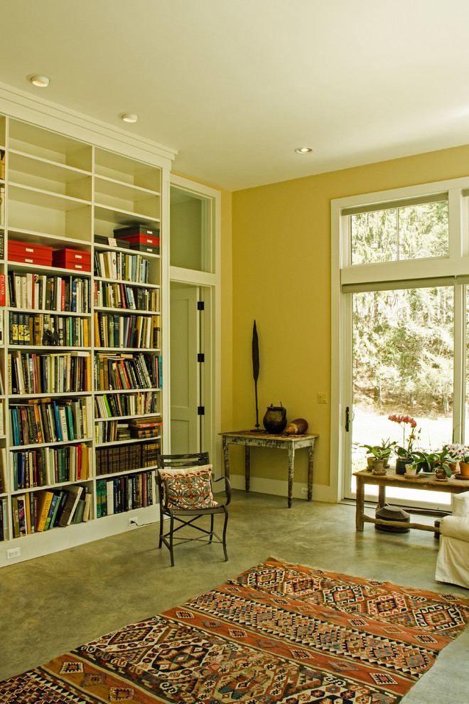 Cette photo montre un salon tendance de taille moyenne et fermé avec une bibliothèque ou un coin lecture, un mur jaune, sol en béton ciré, aucune cheminée et aucun téléviseur.