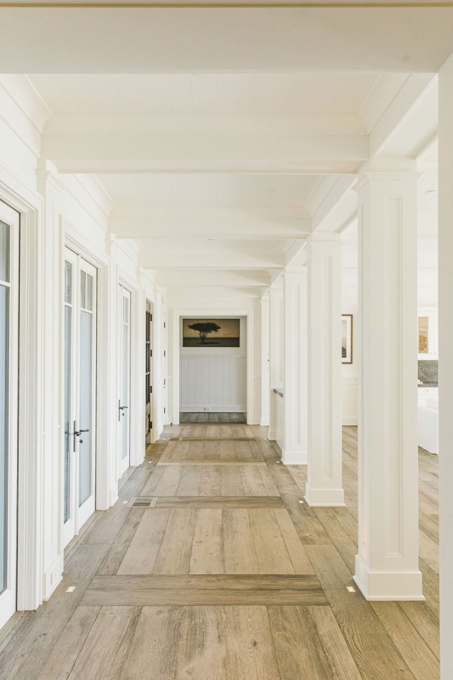 На фото: огромная парадная, открытая гостиная комната в морском стиле с белыми стенами, полом из фанеры, стандартным камином, фасадом камина из камня и белым полом