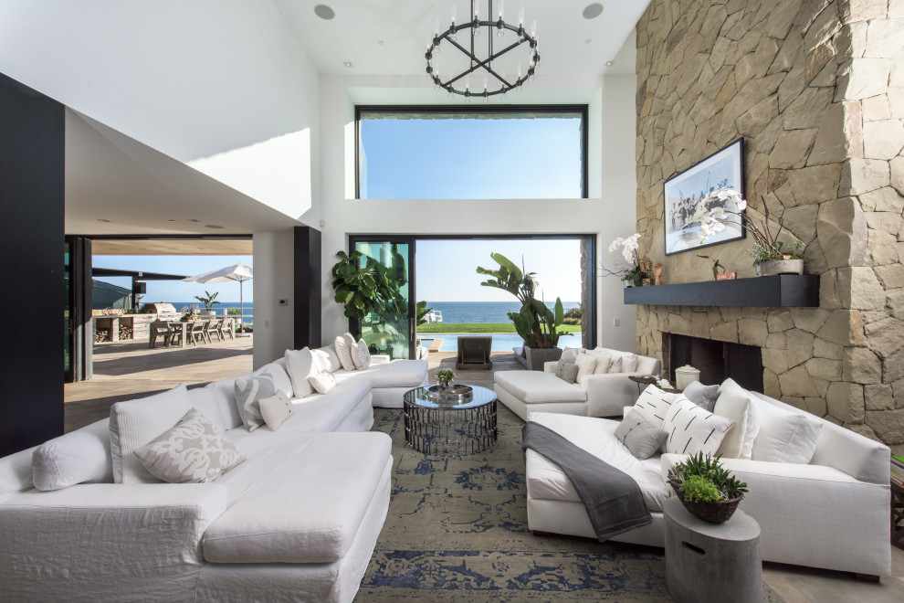 Example of a large trendy open concept porcelain tile, beige floor and vaulted ceiling living room design in Los Angeles with white walls, a standard fireplace, a stone fireplace and no tv