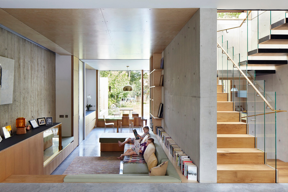 Modelo de biblioteca en casa abierta actual de tamaño medio sin chimenea con paredes grises, suelo de cemento y televisor retractable