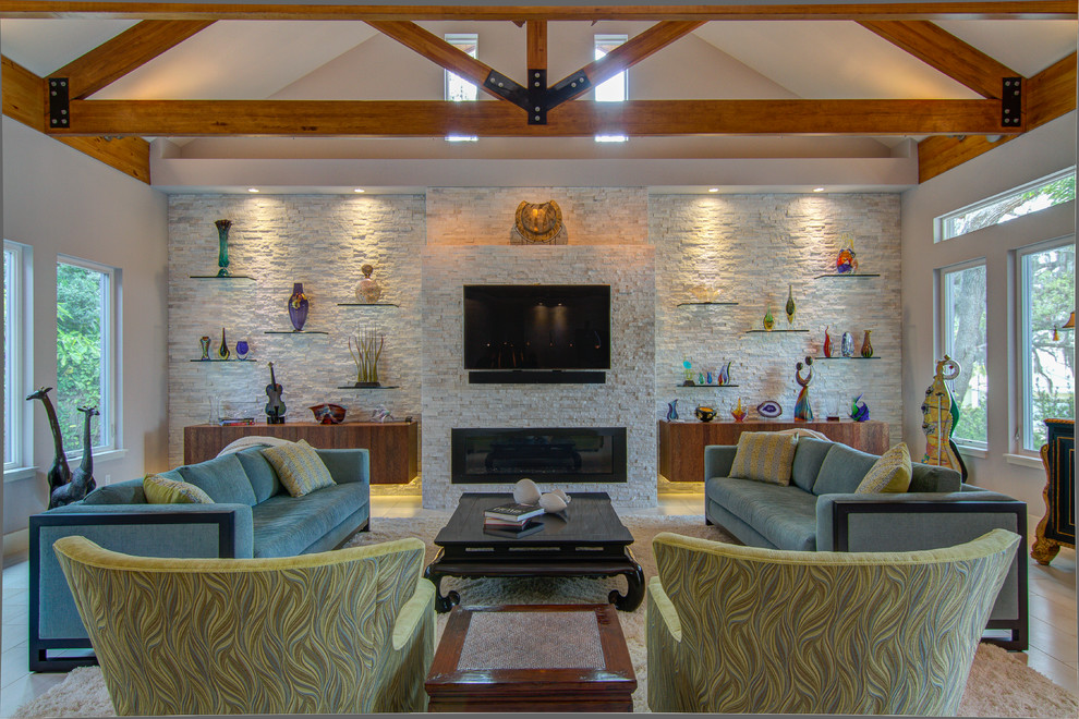 На фото: огромная открытая гостиная комната в современном стиле с горизонтальным камином, фасадом камина из камня, телевизором на стене, полом из керамогранита и синим диваном с
