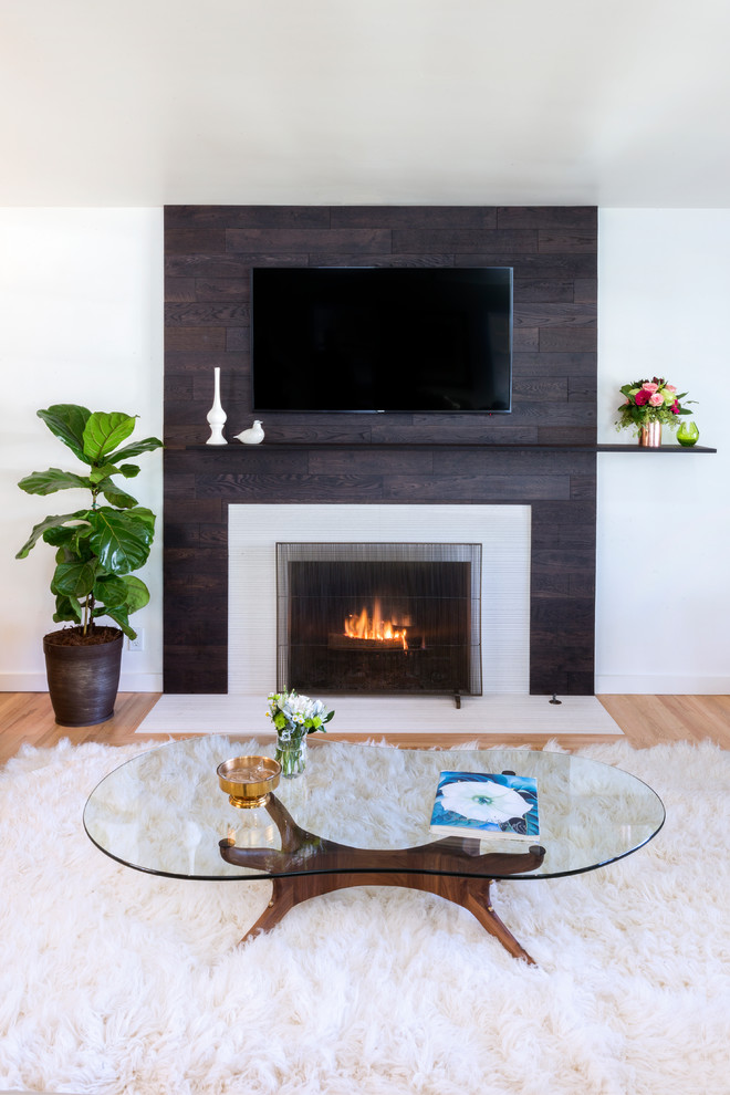 ロサンゼルスにあるお手頃価格の中くらいなミッドセンチュリースタイルのおしゃれなLDK (グレーの壁、淡色無垢フローリング、標準型暖炉、木材の暖炉まわり、壁掛け型テレビ) の写真
