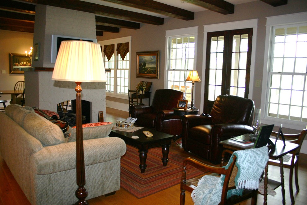 Imagen de salón para visitas cerrado tradicional de tamaño medio con paredes beige, suelo de madera en tonos medios, todas las chimeneas, marco de chimenea de ladrillo y televisor colgado en la pared