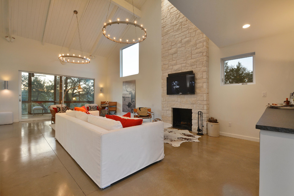 オースティンにある広いコンテンポラリースタイルのおしゃれなLDK (白い壁、コンクリートの床、標準型暖炉、石材の暖炉まわり、壁掛け型テレビ) の写真