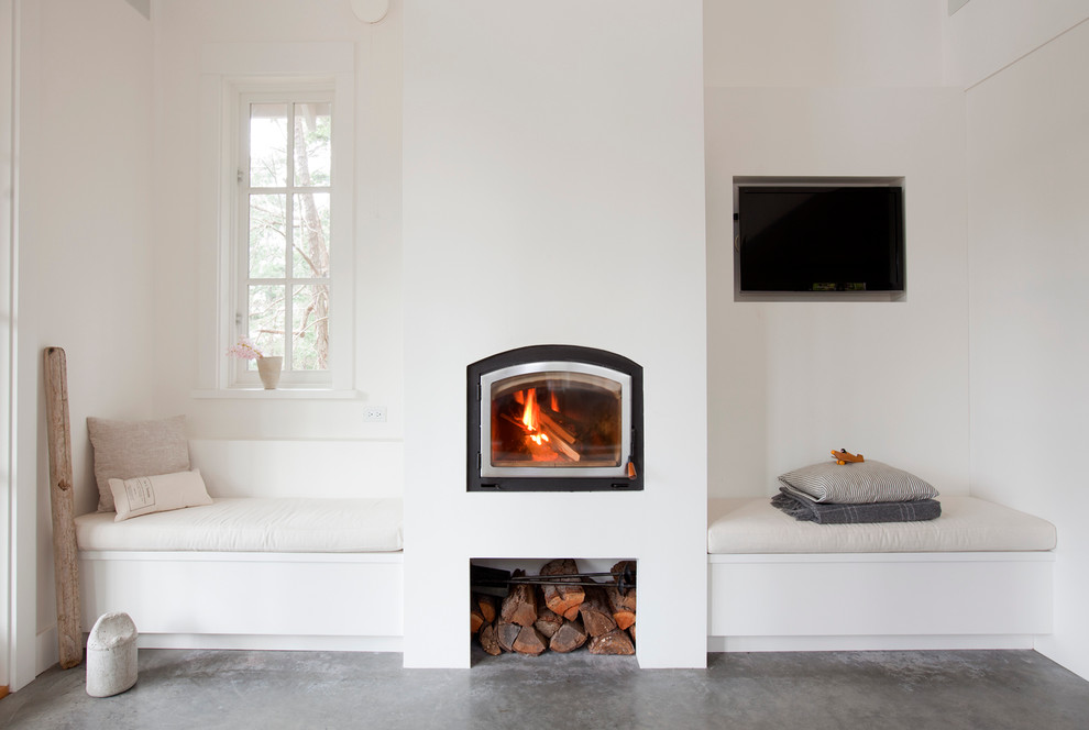 バンクーバーにある北欧スタイルのおしゃれな独立型リビング (白い壁、コンクリートの床、標準型暖炉、漆喰の暖炉まわり、壁掛け型テレビ、グレーの床) の写真