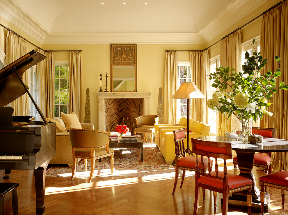 Cette photo montre un salon chic avec une salle de réception, un mur jaune, un sol en bois brun, une cheminée standard et un manteau de cheminée en pierre.