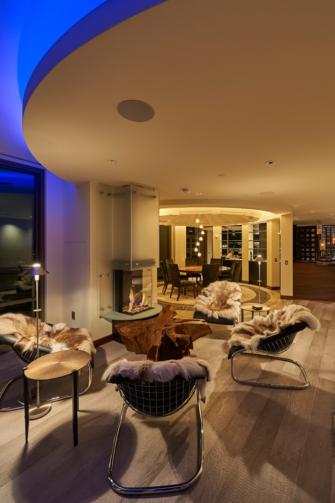 Example of a large trendy open concept light wood floor and gray floor living room design in Other with a two-sided fireplace and a wood fireplace surround