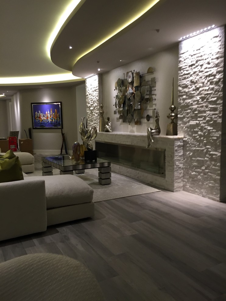 Imagen de salón para visitas abierto actual de tamaño medio sin televisor con paredes beige, suelo de madera clara, chimenea lineal y marco de chimenea de piedra