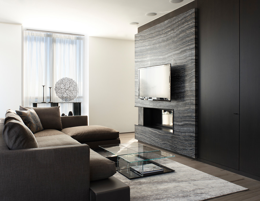 Modelo de salón contemporáneo con paredes negras, chimenea de doble cara, televisor colgado en la pared y suelo marrón
