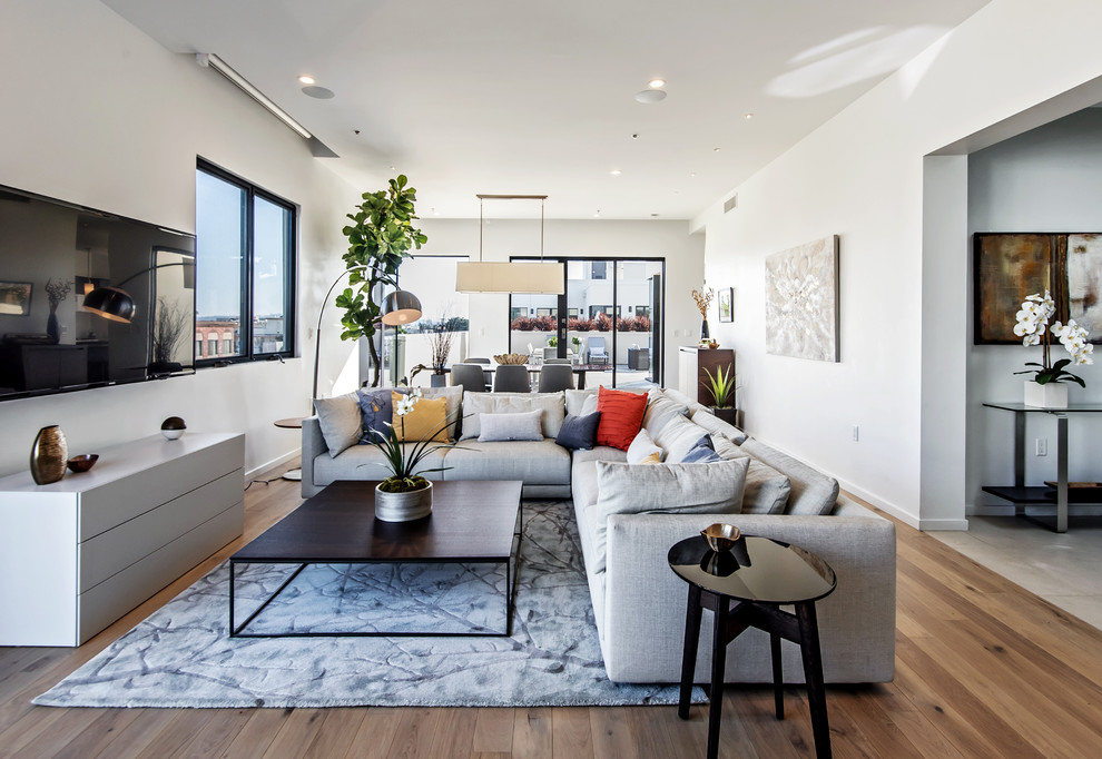 Großes, Offenes Modernes Wohnzimmer mit weißer Wandfarbe, TV-Wand, braunem Holzboden und braunem Boden in Los Angeles