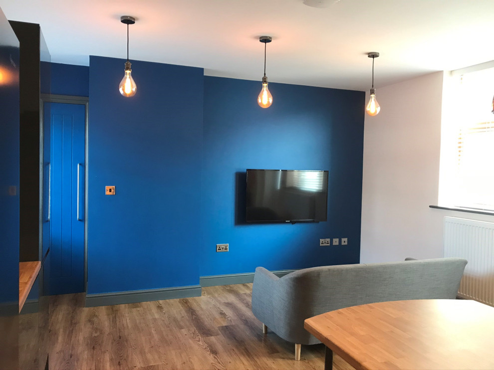 Small modern formal open plan living room in West Midlands with blue walls, laminate floors, no fireplace, a wall mounted tv and brown floors.