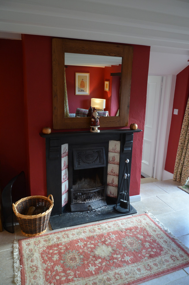 Cette photo montre un petit salon chic fermé avec une bibliothèque ou un coin lecture, un mur rouge, un sol en calcaire, une cheminée standard, un manteau de cheminée en métal, un téléviseur d'angle et poutres apparentes.