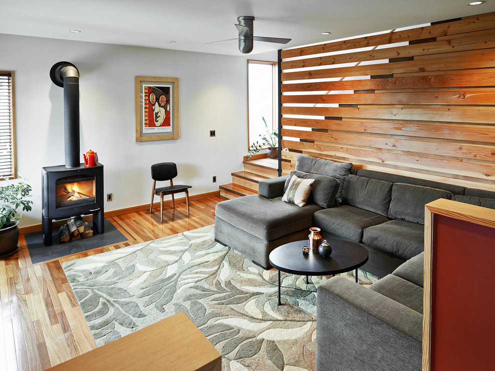 Imagen de salón actual con paredes blancas, suelo de madera en tonos medios y estufa de leña