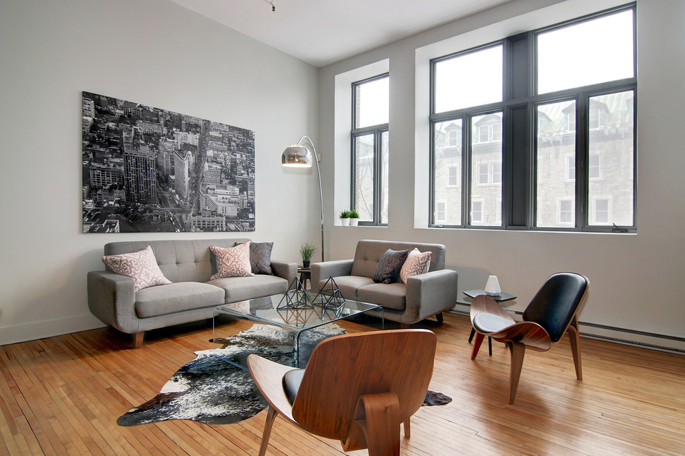 This is an example of a large urban open plan living room in Montreal with grey walls, light hardwood flooring, a wall mounted tv and brown floors.