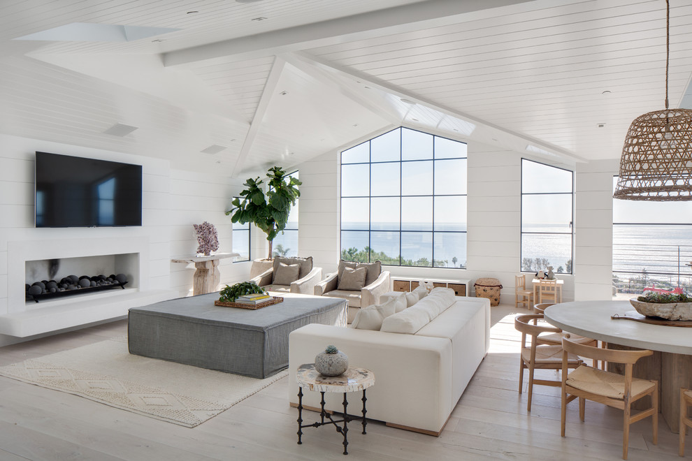 This is an example of a large beach style open plan living room in Orange County with white walls, light hardwood flooring, a ribbon fireplace, a stone fireplace surround, a wall mounted tv, beige floors, a vaulted ceiling, a wood ceiling and tongue and groove walls.