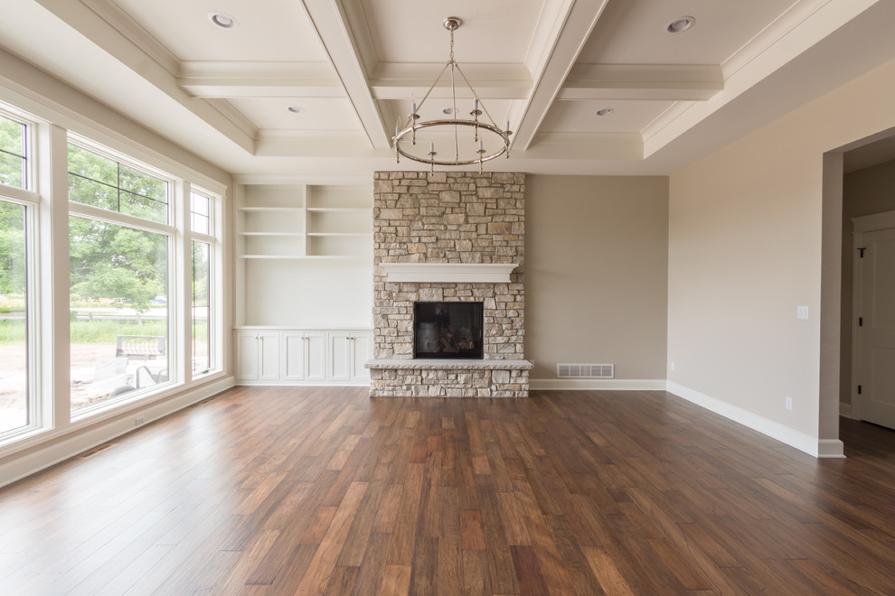 Exemple d'un grand salon nature ouvert avec un mur gris, un sol en bois brun, une cheminée standard, un manteau de cheminée en pierre, un téléviseur encastré et un sol marron.