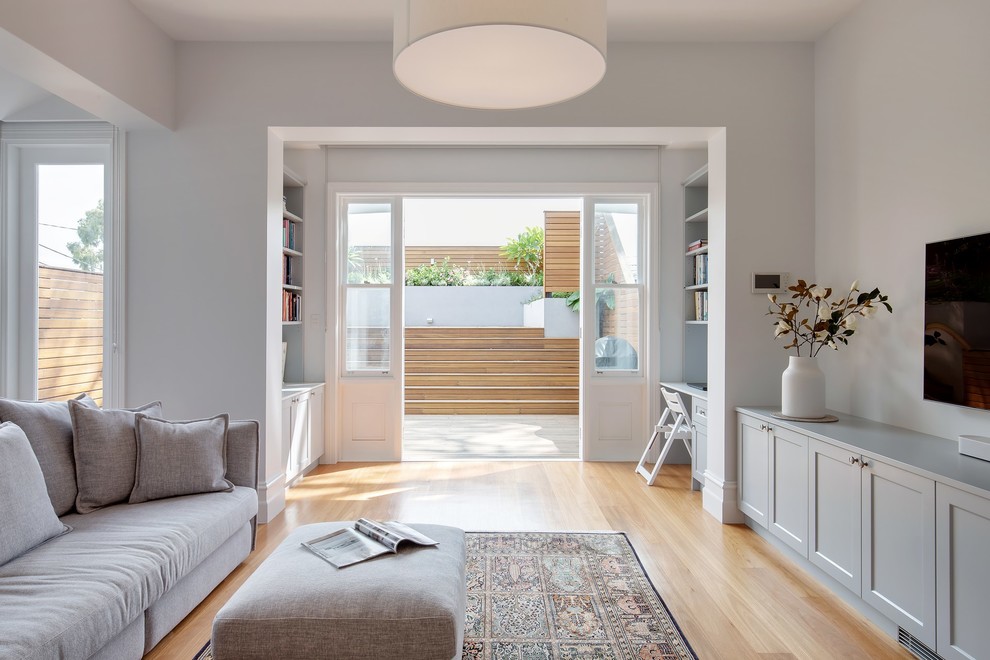 Esempio di un soggiorno stile marinaro di medie dimensioni e aperto con pareti bianche, pavimento in legno massello medio, TV a parete e pavimento marrone