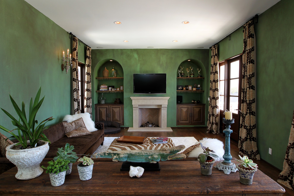 Источник вдохновения для домашнего уюта: большая парадная, изолированная гостиная комната в средиземноморском стиле с зелеными стенами, темным паркетным полом, телевизором на стене, стандартным камином, фасадом камина из камня и коричневым полом