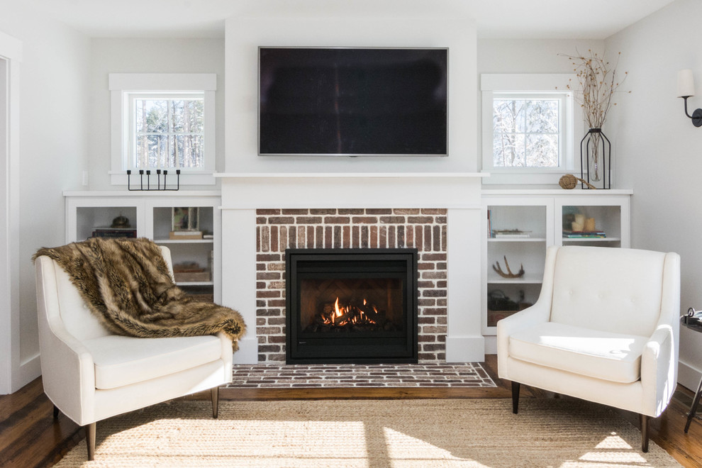ポートランド(メイン)にある中くらいなカントリー風のおしゃれなLDK (白い壁、無垢フローリング、標準型暖炉、レンガの暖炉まわり、壁掛け型テレビ、茶色い床) の写真