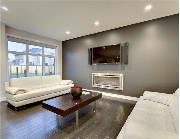 Идея дизайна: открытая гостиная комната в современном стиле с серыми стенами, темным паркетным полом, горизонтальным камином, фасадом камина из металла и телевизором на стене