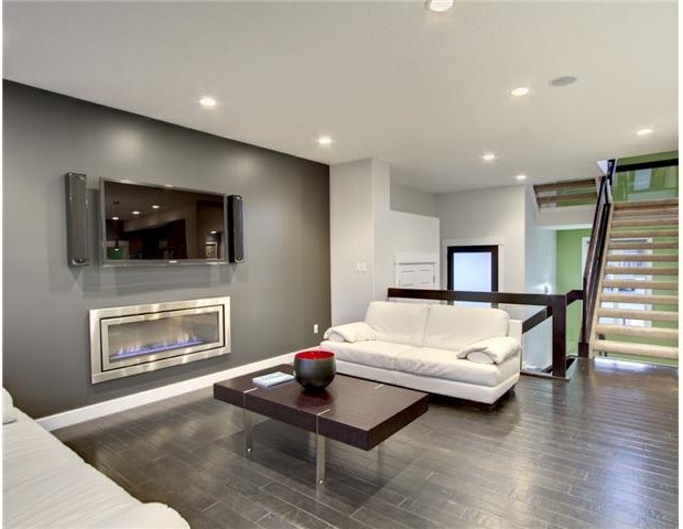 Foto de salón abierto actual con paredes grises, suelo de madera oscura, chimenea lineal, marco de chimenea de metal y televisor colgado en la pared