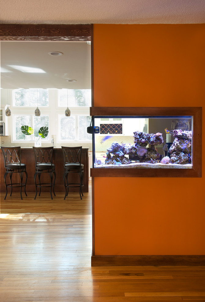На фото: открытая гостиная комната среднего размера в стиле неоклассика (современная классика) с оранжевыми стенами, светлым паркетным полом, двусторонним камином, фасадом камина из кирпича и телевизором на стене с