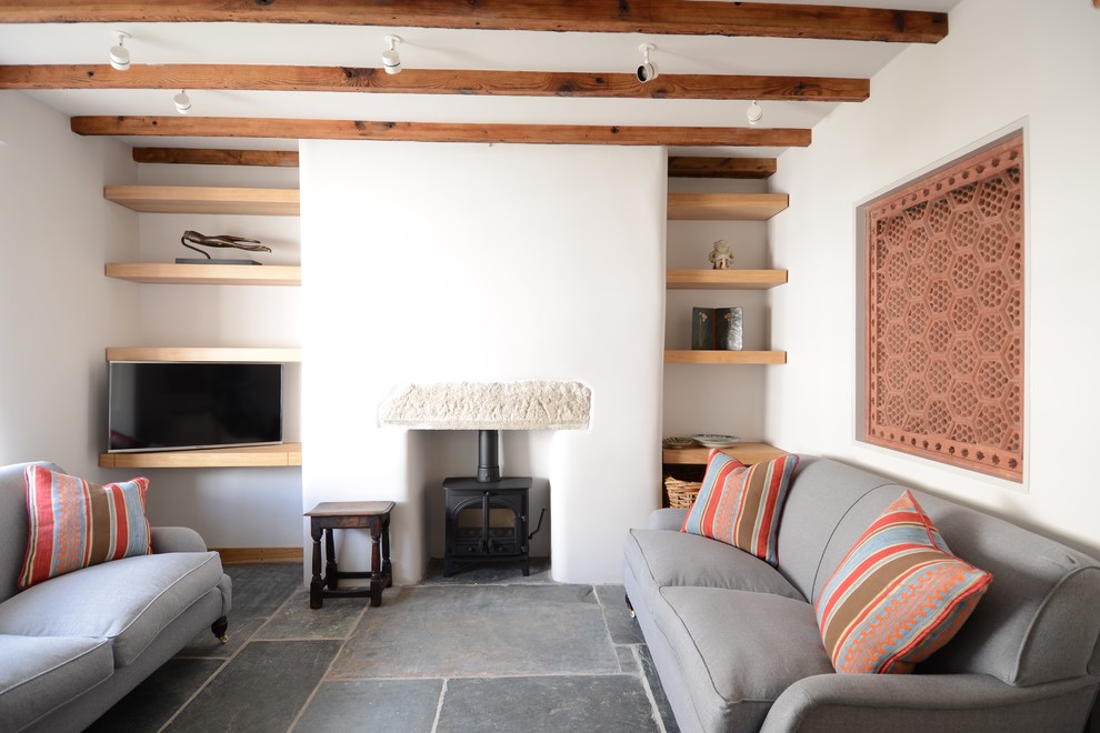 Modelo de salón cerrado rural pequeño con paredes blancas, suelo de pizarra, estufa de leña, marco de chimenea de yeso y televisor independiente