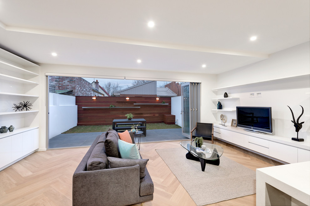 This is an example of a contemporary open plan living room in Melbourne with white walls, medium hardwood flooring and a freestanding tv.