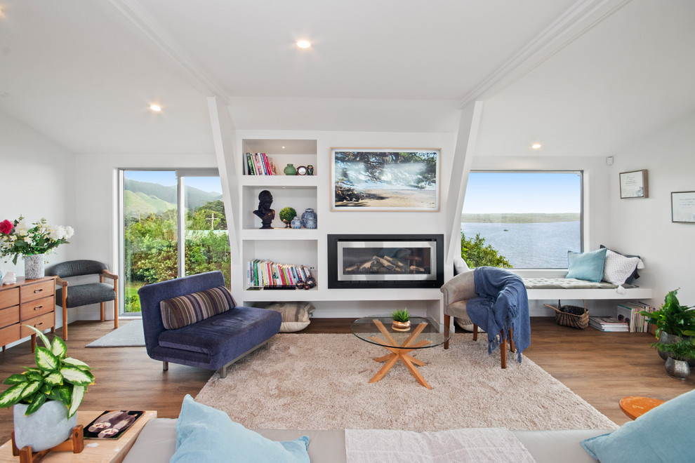 This is an example of an expansive contemporary open plan living room in Auckland with white walls, medium hardwood flooring, a metal fireplace surround, a wall mounted tv, brown floors and a ribbon fireplace.