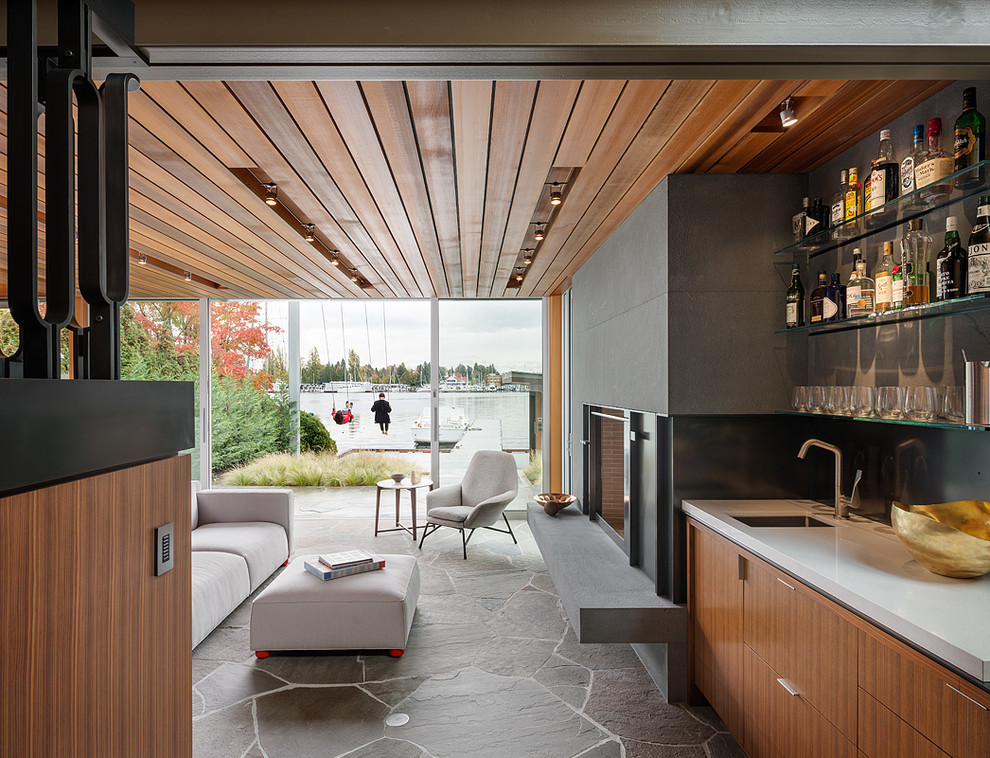 Cette image montre un salon minimaliste avec un bar de salon, un sol en ardoise, une cheminée standard, un manteau de cheminée en pierre et un téléviseur dissimulé.