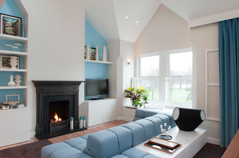 На фото: парадная гостиная комната в стиле неоклассика (современная классика) с бежевыми стенами, стандартным камином, отдельно стоящим телевизором и синим диваном с
