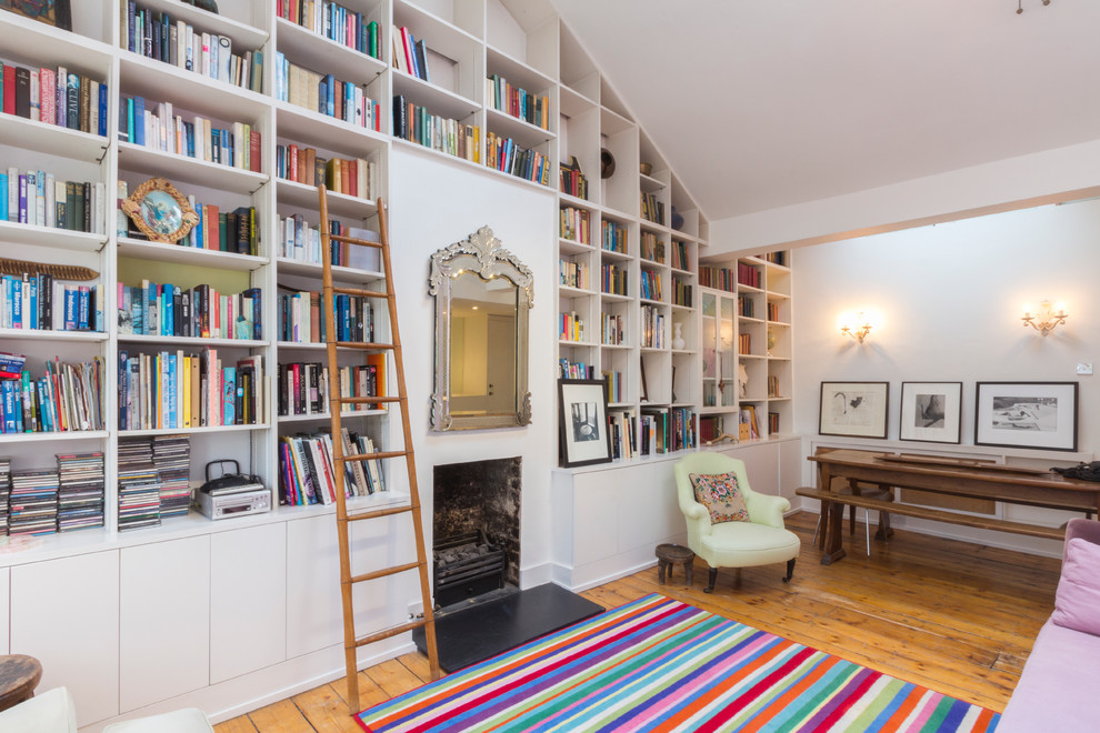 Idée de décoration pour un salon design ouvert avec une bibliothèque ou un coin lecture, un mur blanc, un sol en bois brun et une cheminée standard.