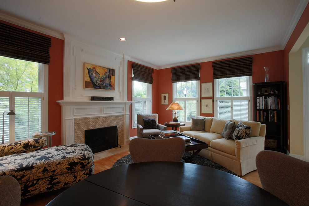Пример оригинального дизайна: большая открытая гостиная комната в стиле неоклассика (современная классика) с оранжевыми стенами, светлым паркетным полом, стандартным камином, фасадом камина из плитки и с книжными шкафами и полками