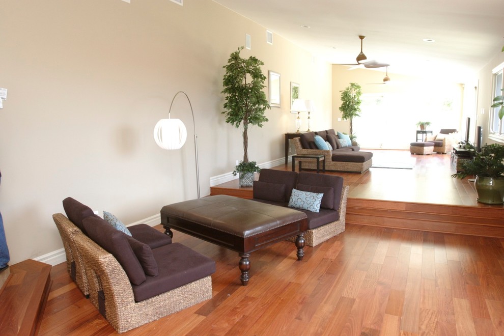 Modelo de salón abierto tropical grande sin chimenea con paredes beige, suelo de madera en tonos medios y televisor independiente