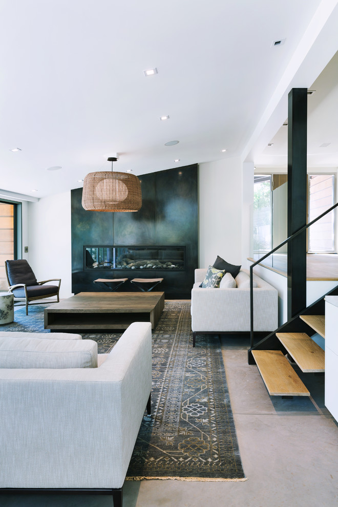 Cette image montre un salon design avec sol en béton ciré et un manteau de cheminée en métal.