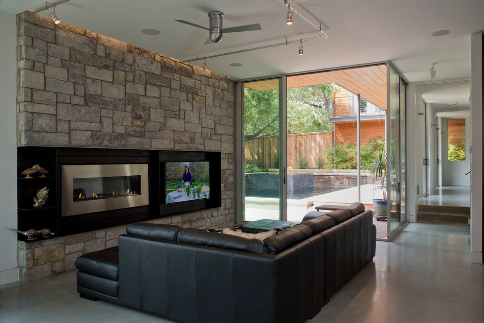 Diseño de salón abierto contemporáneo de tamaño medio con paredes blancas, suelo de cemento, chimenea lineal, marco de chimenea de piedra y pared multimedia