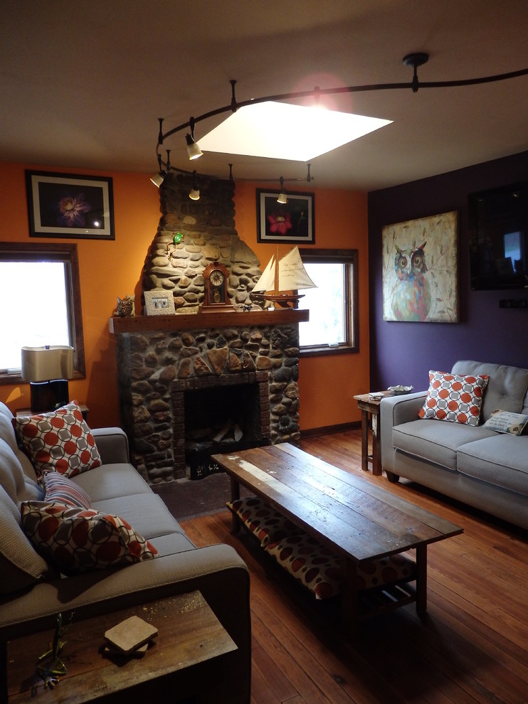 Imagen de salón para visitas cerrado ecléctico pequeño con paredes multicolor, suelo de madera en tonos medios, chimenea de doble cara, marco de chimenea de piedra y televisor colgado en la pared