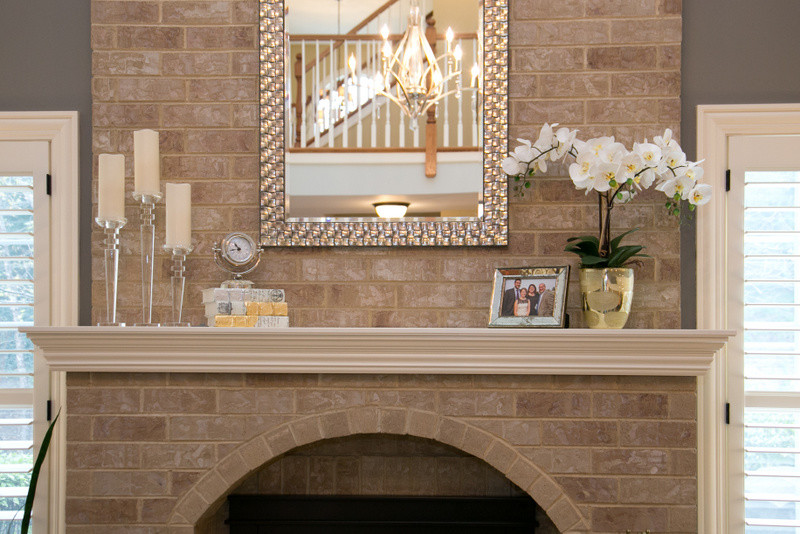 На фото: открытая гостиная комната среднего размера в стиле неоклассика (современная классика) с серыми стенами, ковровым покрытием, стандартным камином, фасадом камина из кирпича и скрытым телевизором с