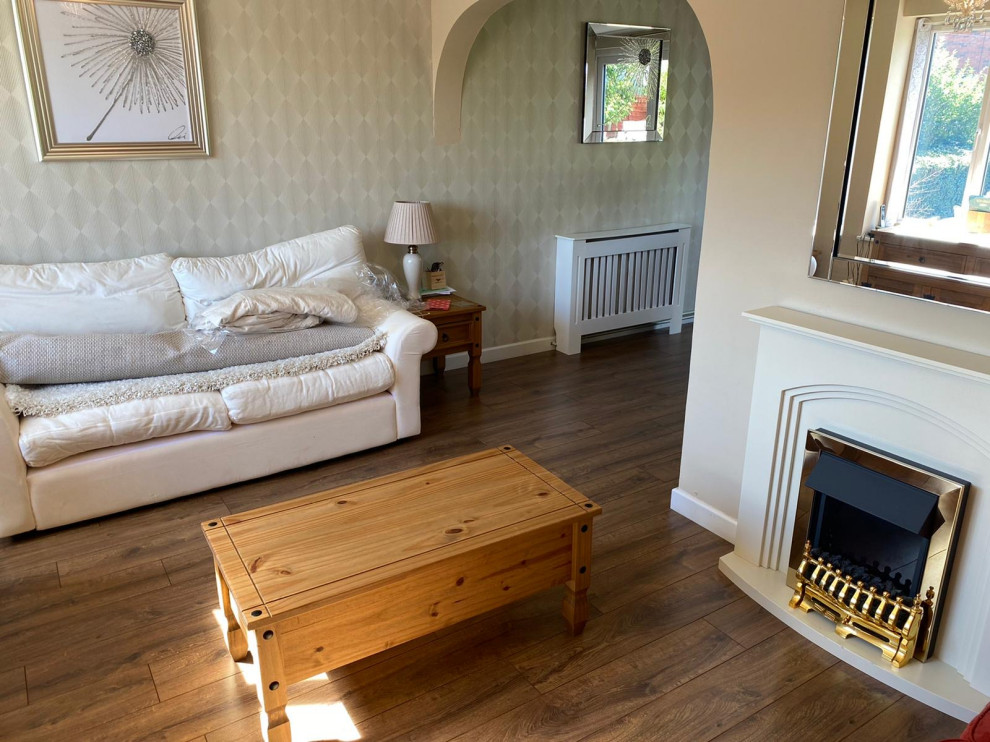Bild på ett litet separat vardagsrum, med beige väggar, ljust trägolv, en standard öppen spis, en spiselkrans i trä och brunt golv