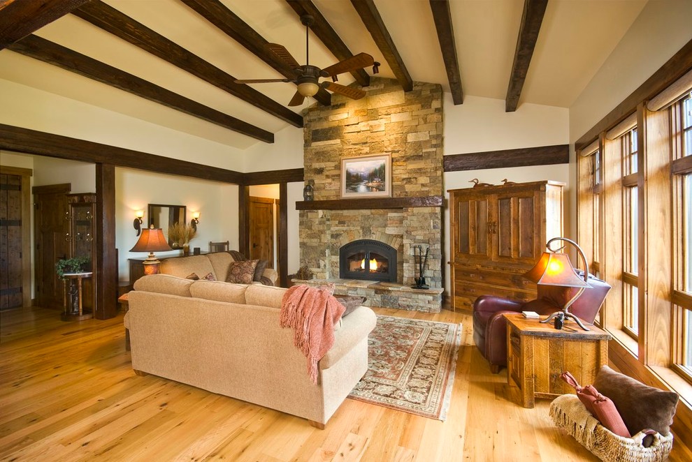 Offenes Rustikales Wohnzimmer mit beiger Wandfarbe, hellem Holzboden, Kamin, Kaminumrandung aus Stein und Eck-TV in Boise