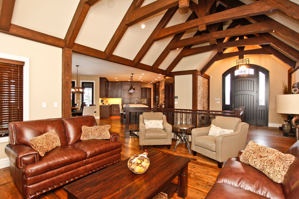 Großes, Fernseherloses, Offenes Rustikales Wohnzimmer mit beiger Wandfarbe, braunem Holzboden, Kamin und Kaminumrandung aus Stein in Calgary