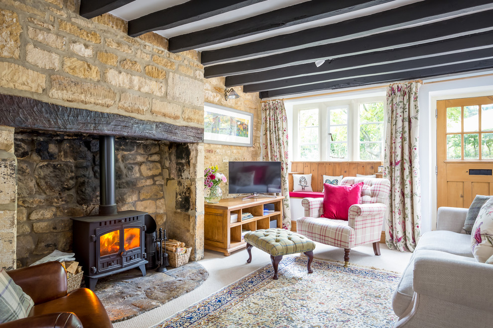 Large farmhouse enclosed living room in Gloucestershire with white walls, carpet, a wood burning stove, a stone fireplace surround and a freestanding tv.