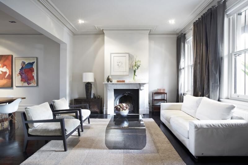 Источник вдохновения для домашнего уюта: гостиная комната в стиле неоклассика (современная классика) с белыми стенами, темным паркетным полом, стандартным камином и фасадом камина из камня