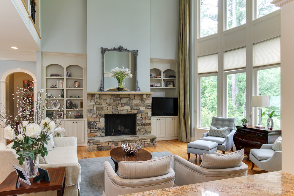 Design ideas for a large classic formal open plan living room in Raleigh with blue walls, light hardwood flooring, a standard fireplace, a stone fireplace surround, a built-in media unit and beige floors.