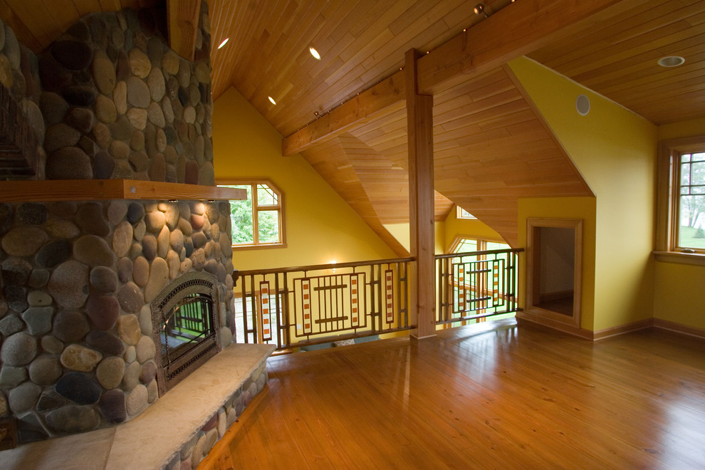Rustik inredning av ett stort loftrum, med ett finrum, gula väggar, mellanmörkt trägolv, en öppen hörnspis, en spiselkrans i sten och brunt golv