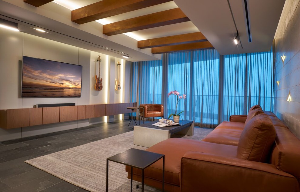 На фото: большая изолированная гостиная комната в современном стиле с бежевыми стенами, полом из сланца, телевизором на стене и серым полом без камина с