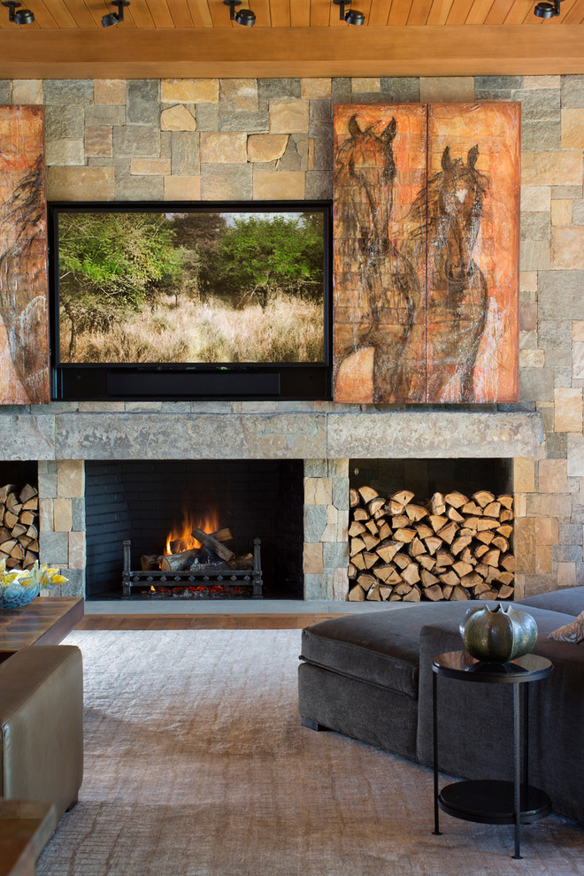 Foto de salón abierto actual con suelo de madera en tonos medios, todas las chimeneas, marco de chimenea de piedra y televisor retractable