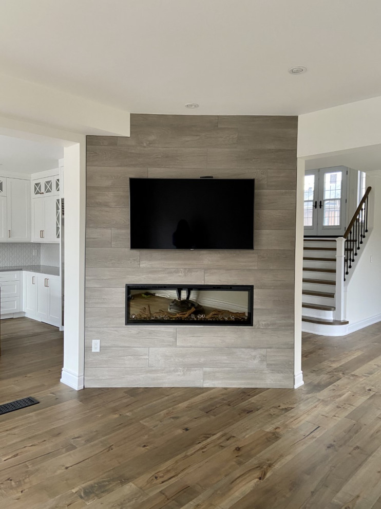 Esempio di un soggiorno classico aperto con pareti bianche, pavimento in legno massello medio, cornice del camino piastrellata e TV a parete