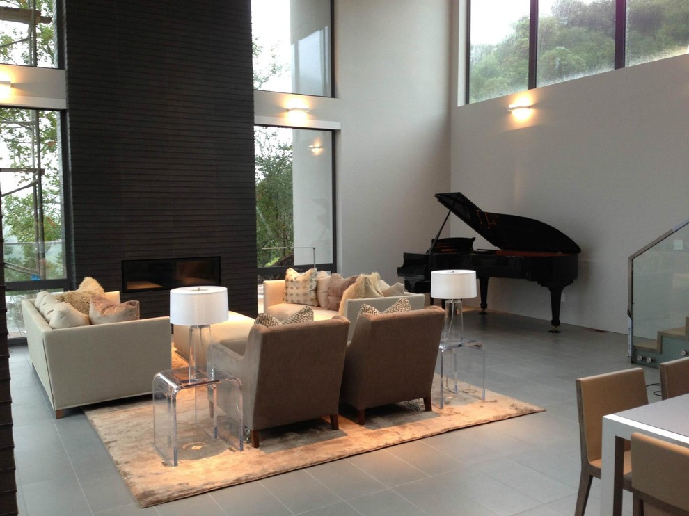 На фото: большая парадная, открытая гостиная комната в стиле модернизм с серыми стенами, полом из керамической плитки, стандартным камином, фасадом камина из плитки и скрытым телевизором с